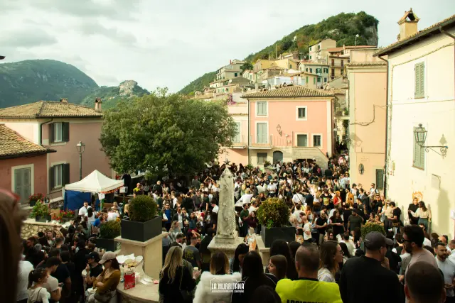 Vista dall'alto della piazza centrale gremita di visitatori con monumento e borgo sullo sfondo