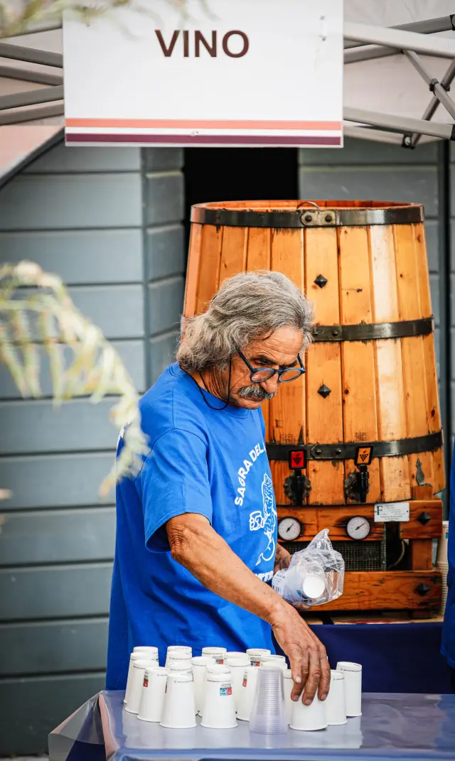 Volontario che serve vino da una grande botte di legno sotto il cartello "Vino"